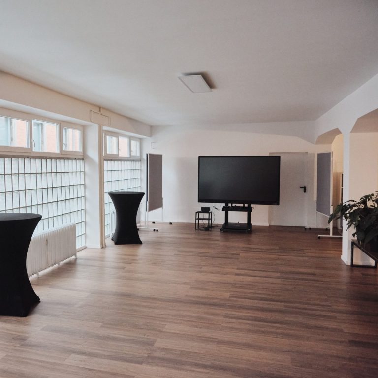 Moderne, helle Innenraum mit Holzfußboden, TV und zwei Stehtischen.
