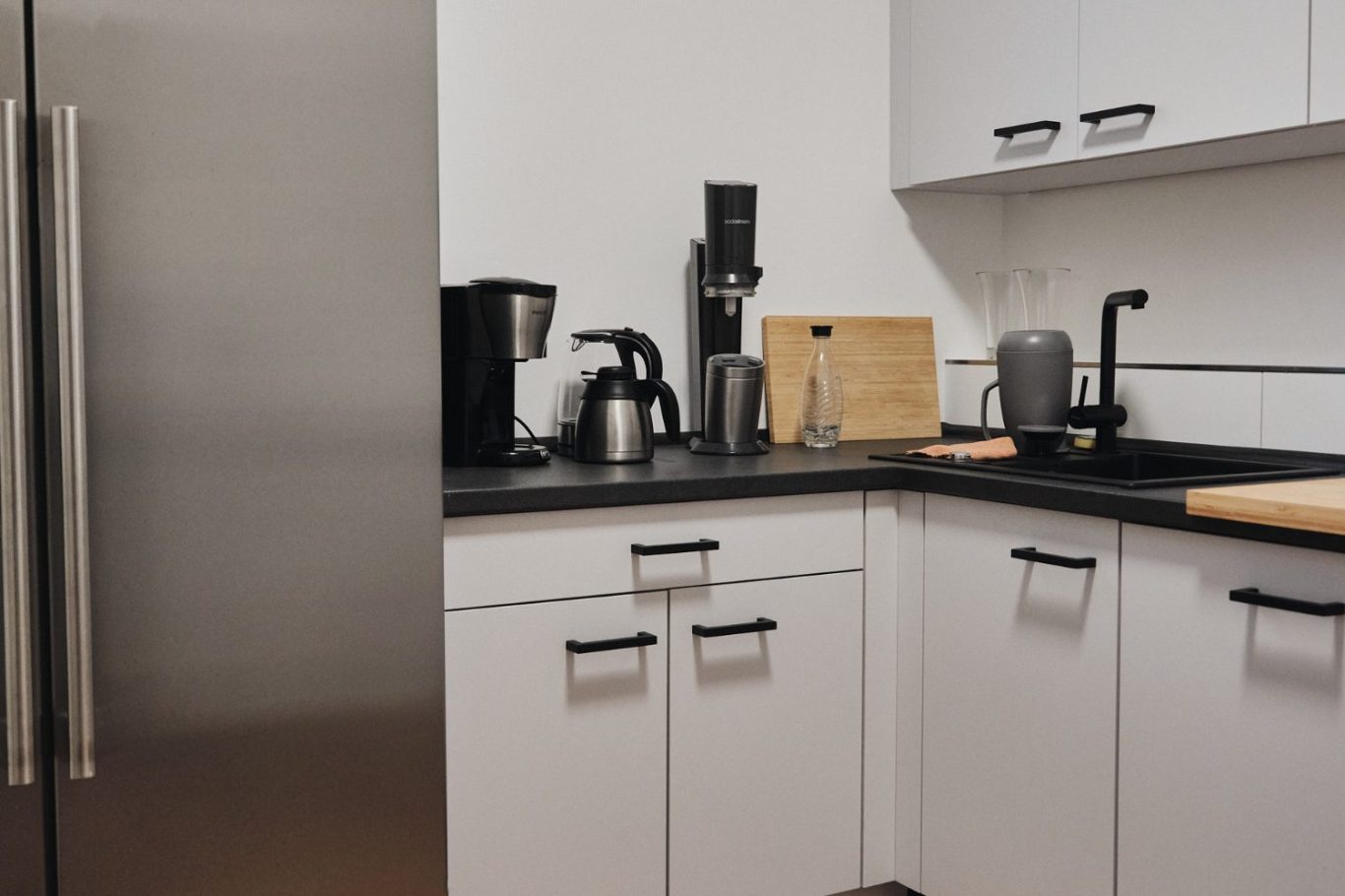 Moderne Küche mit Edelstahl-Geräten, Kaffeeautomaten und Holzschneidebrett.