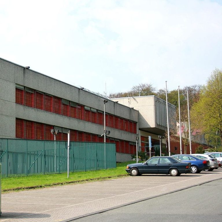 Moderne graue Gebäude mit roten Fensterläden und Parkplätzen davor.