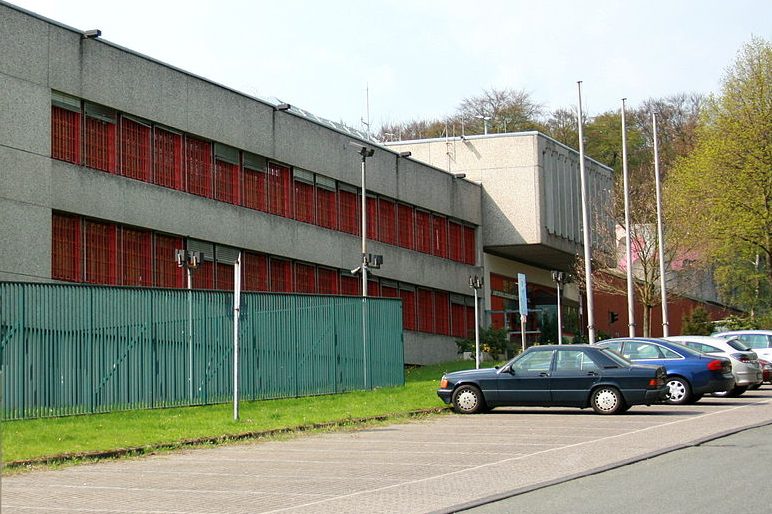 Ein modernes Gebäudekomplex mit rotem Fensterrahmen und parkenden Autos.