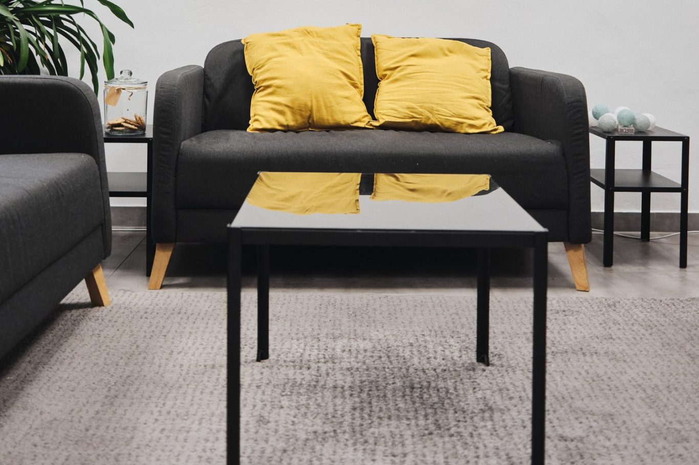 Schwarzer Tisch vor einer couch mit gelben Kissen, umgeben von Pflanzen.