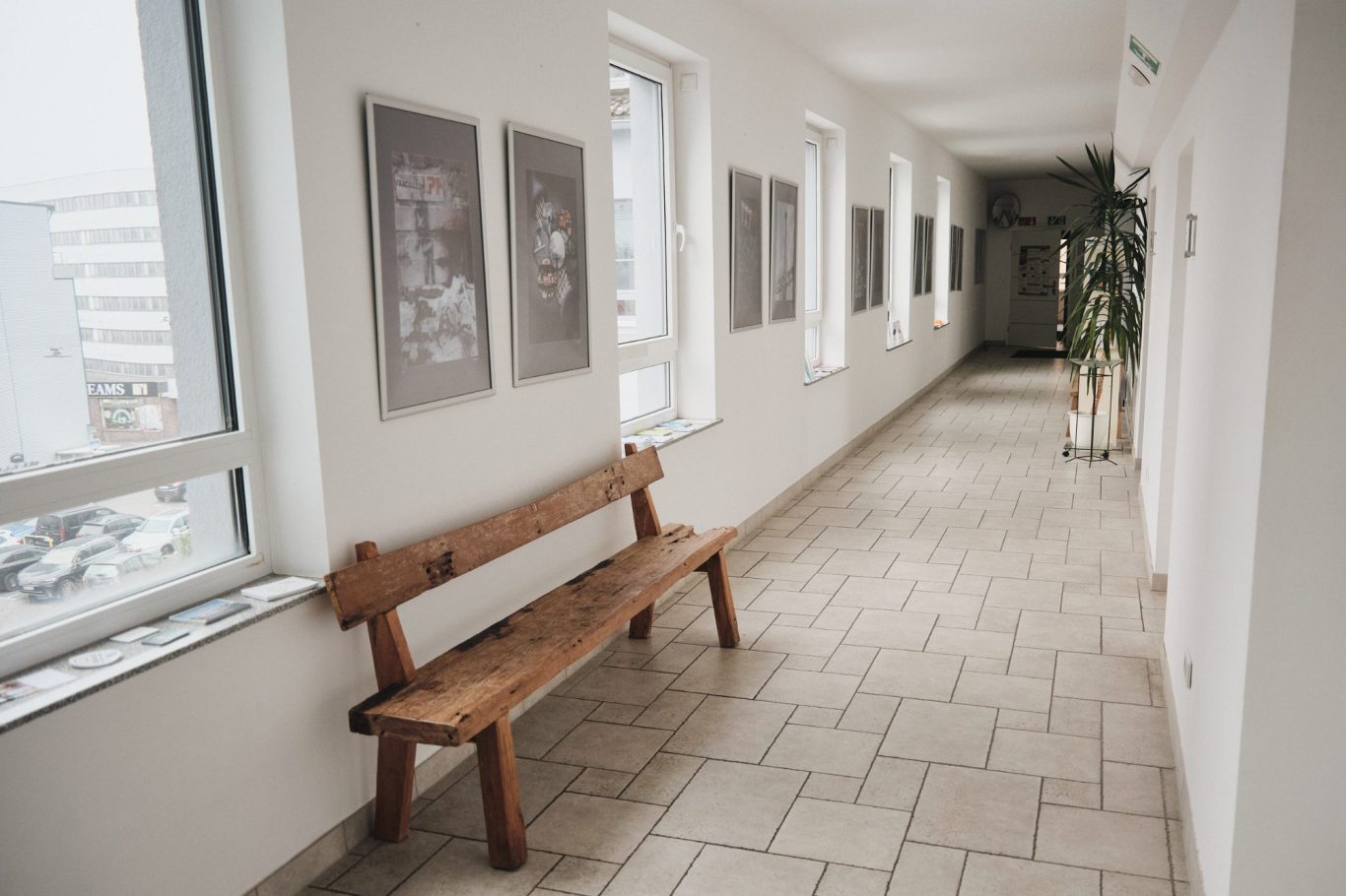 Langer Flur mit Holzbänken und Bildern an den Wänden. Fenster sorgen für Tageslicht.