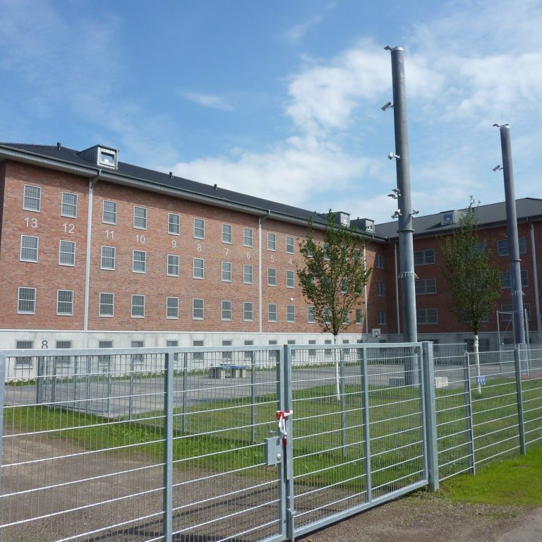 Hintergrund eines Gefängnisses mit grauem Zaun und blauen Himmel.