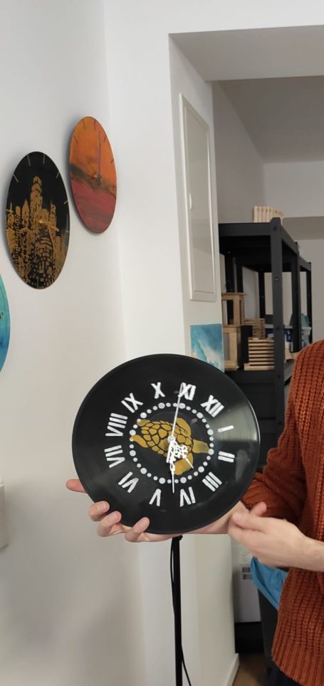 Eine Person hält eine Wanduhr mit einem schwarz-goldenen Ziffernblatt.