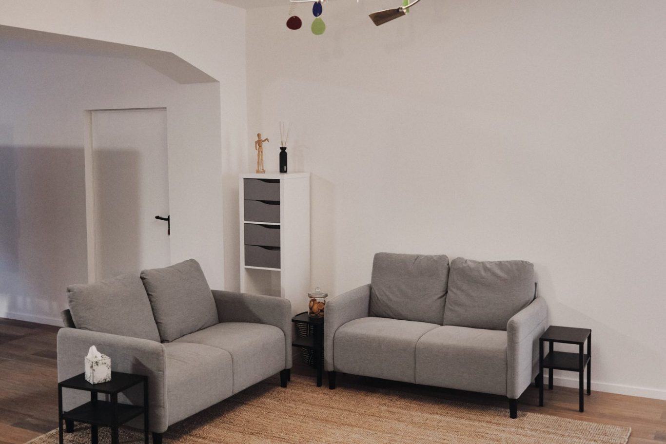 Zwei graue Sofas stehen in einem hellen Raum mit Holzfußboden und minimalistischer Dekoration.