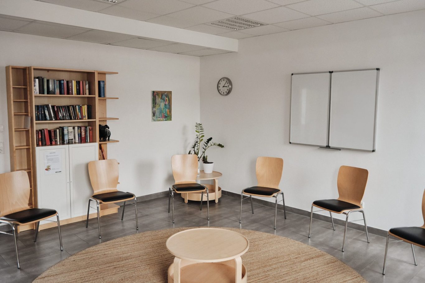 Leerer Raum mit Stuhlkreis, Tisch, Bücherregal und Wandtafel.