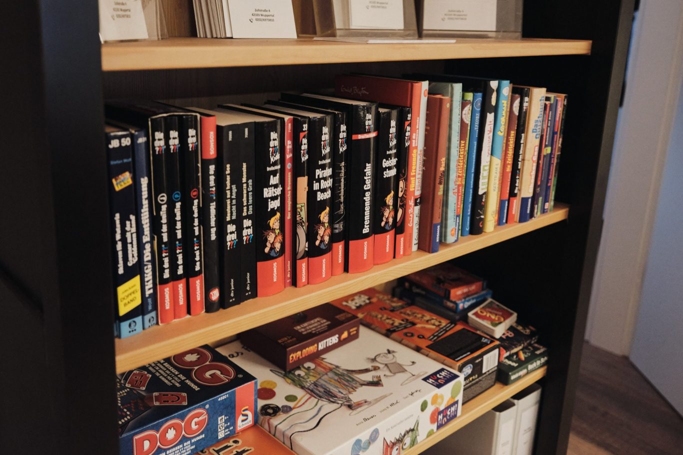 Regal mit verschiedenen Bücherreihen und Brettspielen in unterschiedlichen Größen.