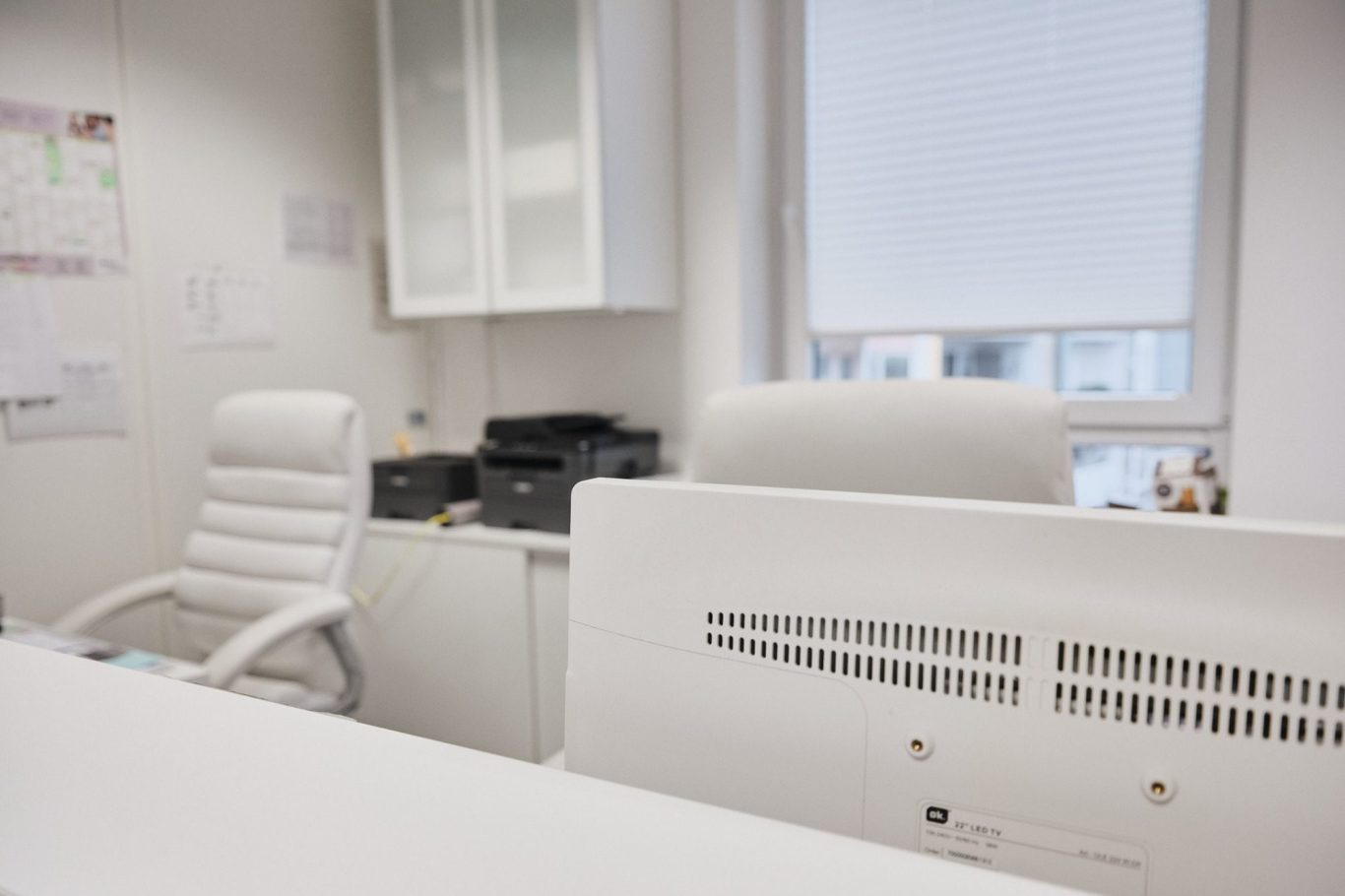 Büro mit einem weißen Schreibtisch, Stuhl und Druckern im Hintergrund.